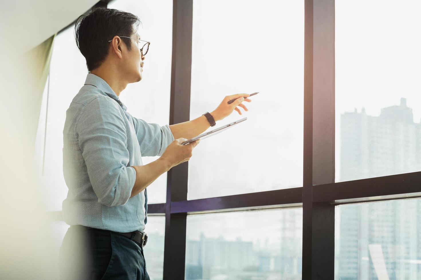 Businessman holding tablet and pointing his finger out of office window. photo