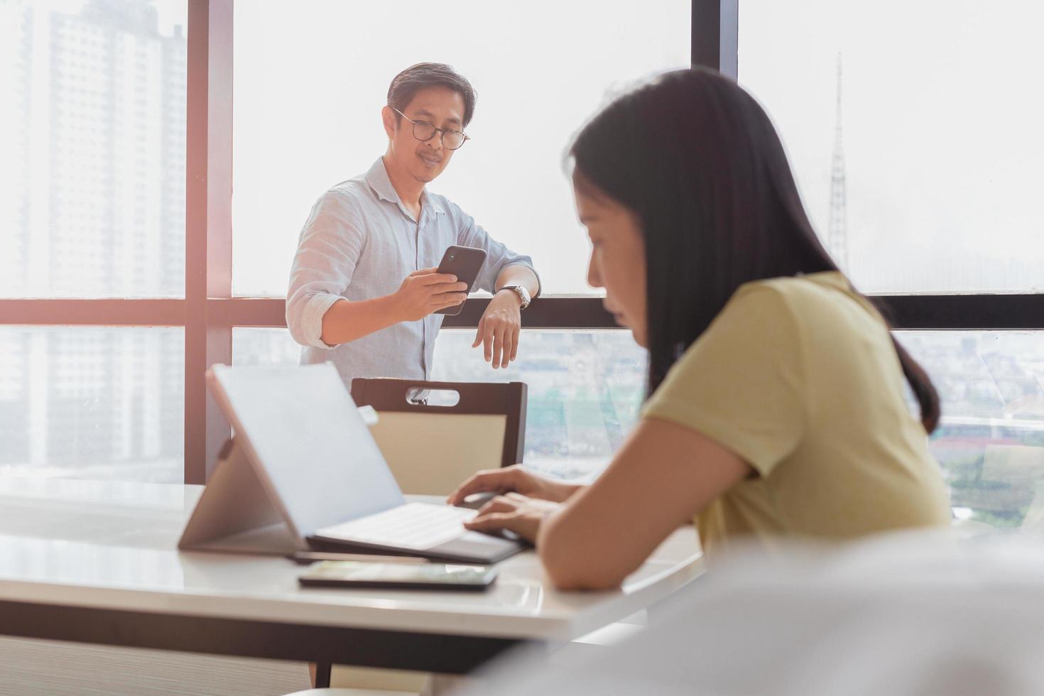 Businessman using cell phone with woman working on laptop in foreground. photo