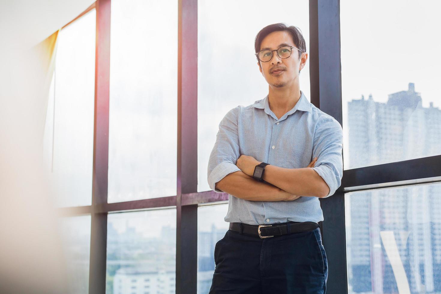 Portrait of business man standing next to office window with arms crossed. photo