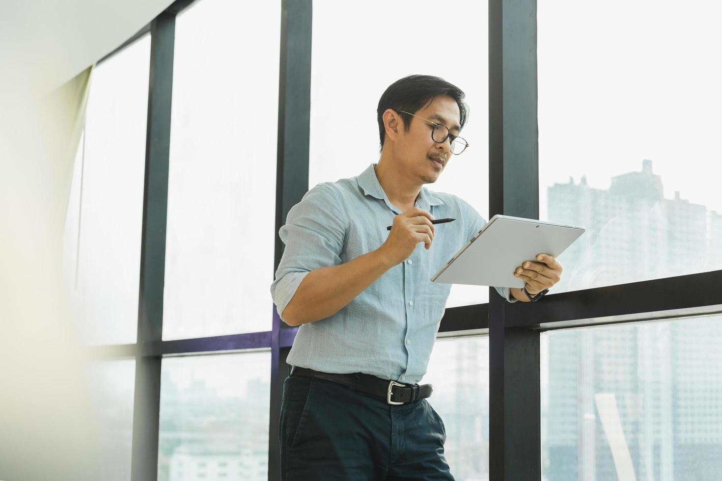 Businessman working online with digital tablet while standing next to office window. photo