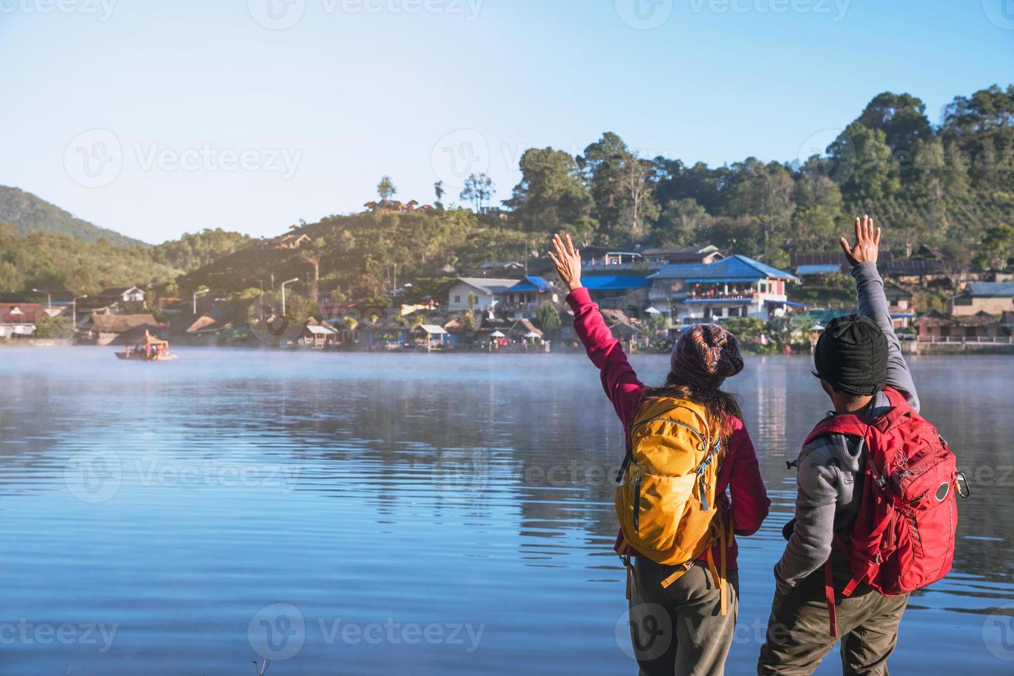 Asian woman and Asian man which backpacking standing near the lake, she was smiling, happy and enjoying the natural beauty of the mist. photo