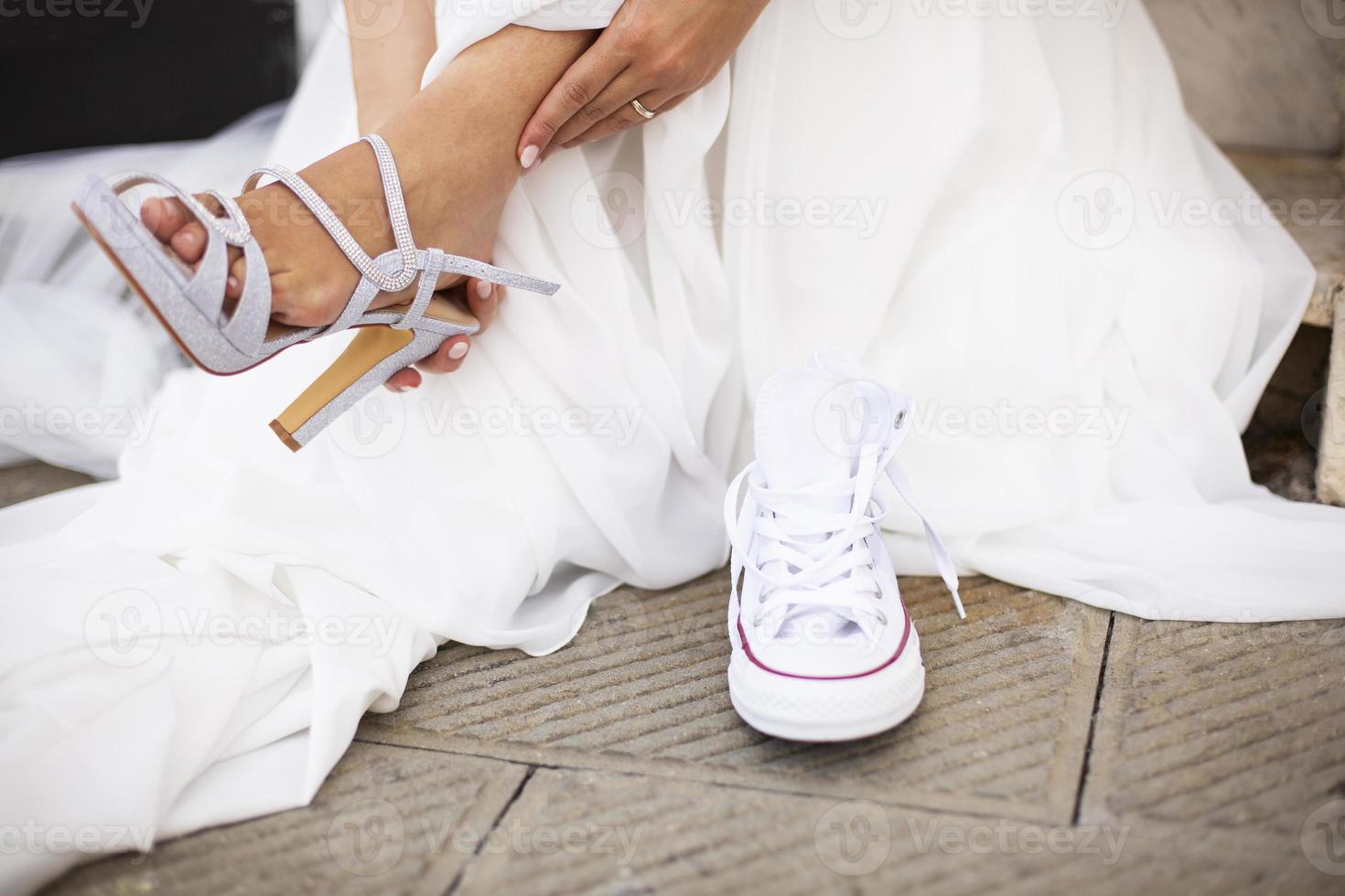 Bride changing her formal shoes with comfortable white sneakers photo