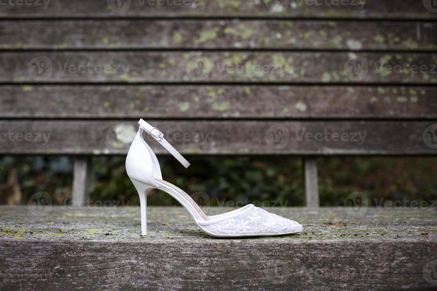 Single bridal shoe seen in profile and placed on ruined wood outdoors photo