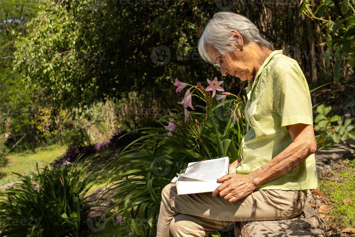 Retrato de perfil de una mujer mayor leyendo un libro en un jardín. foto