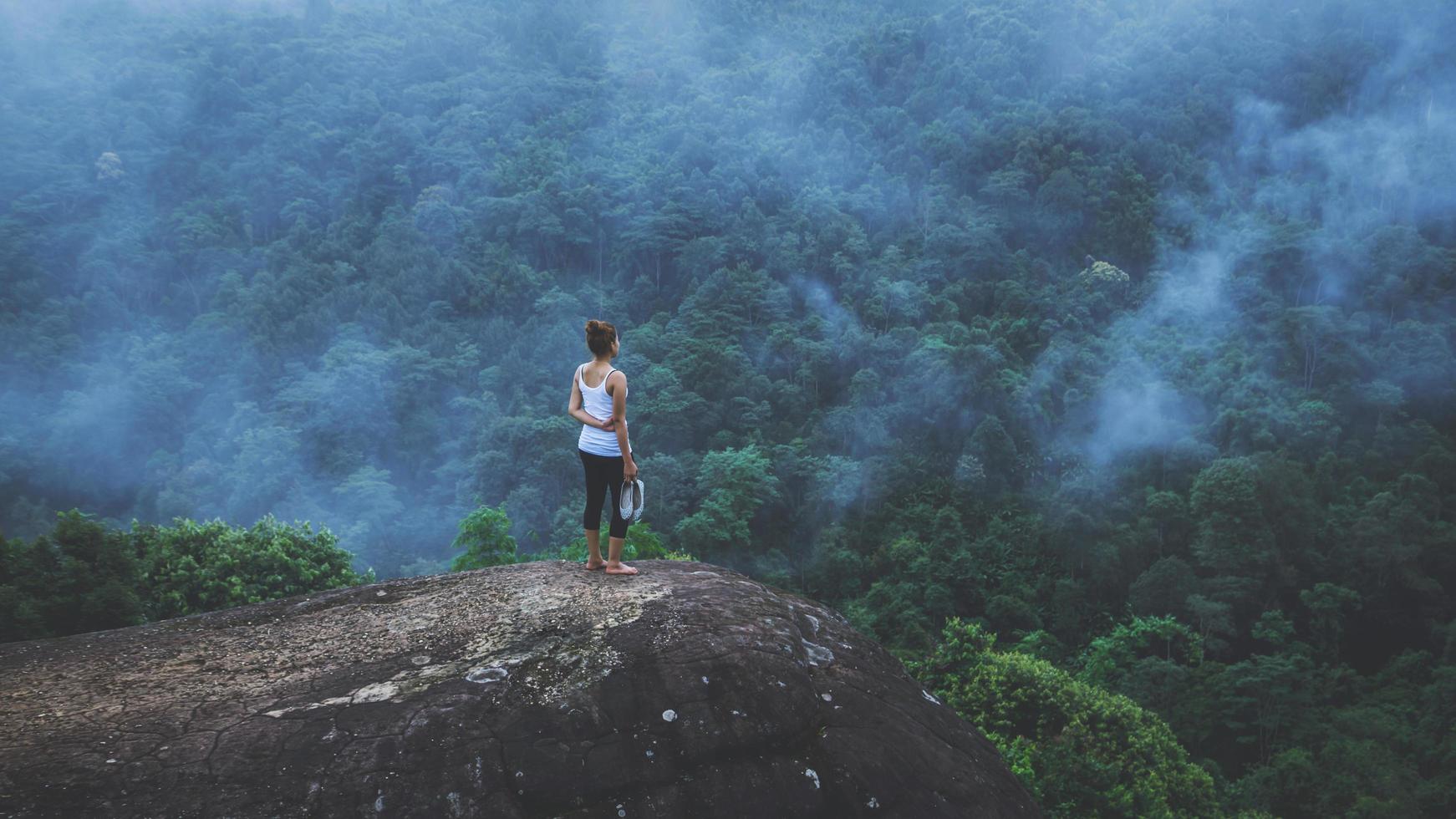 mujer joven ejercita yoga en las montañas. naturaleza de viaje de mujer asiática. viajes relajarse ejercicios yoga touch niebla natural en el pico de la montaña. foto