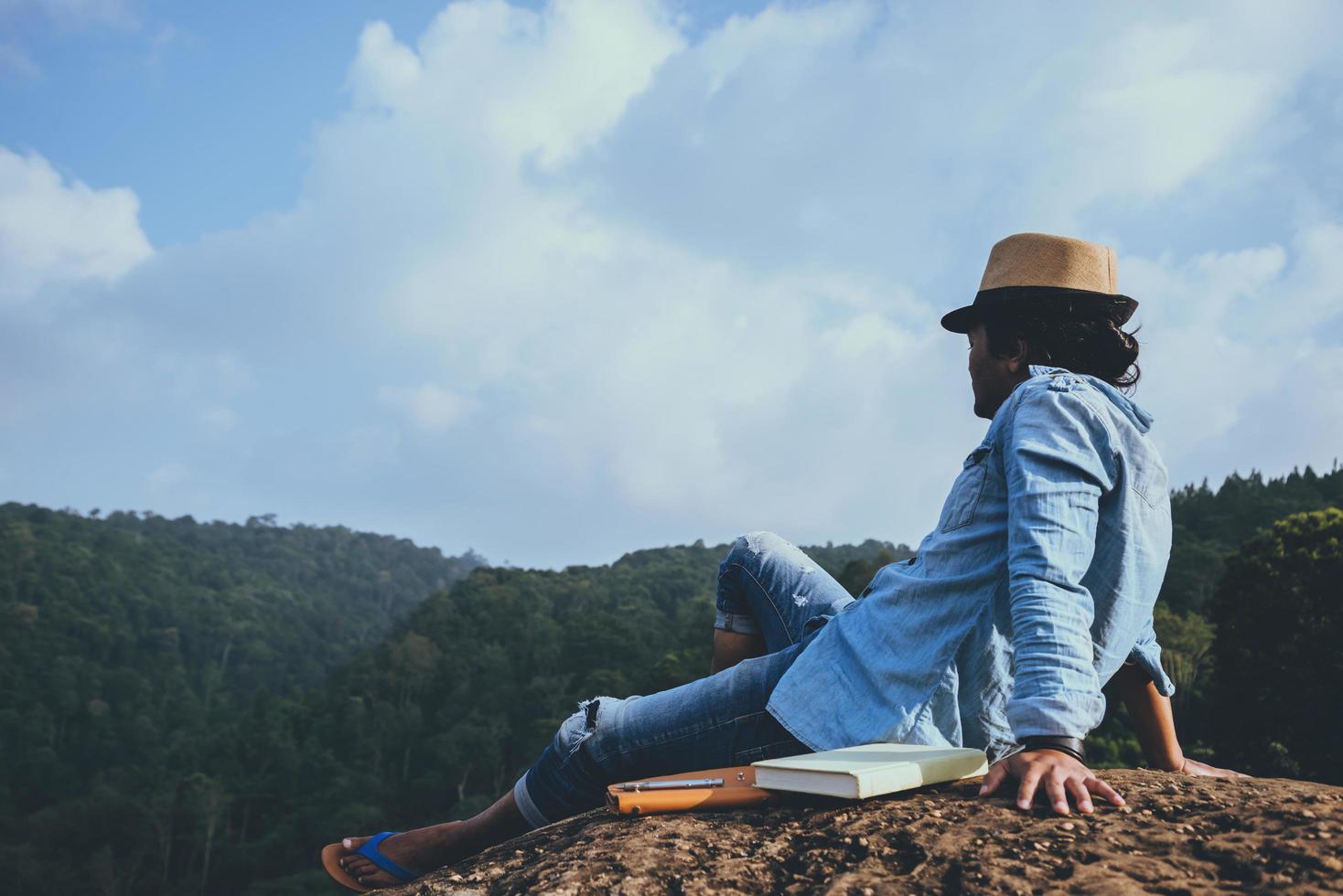 viaje de hombre asiático relajarse en las vacaciones. asientos relajarse leer libros sobre acantilados rocosos. en la montaña. En Tailandia foto