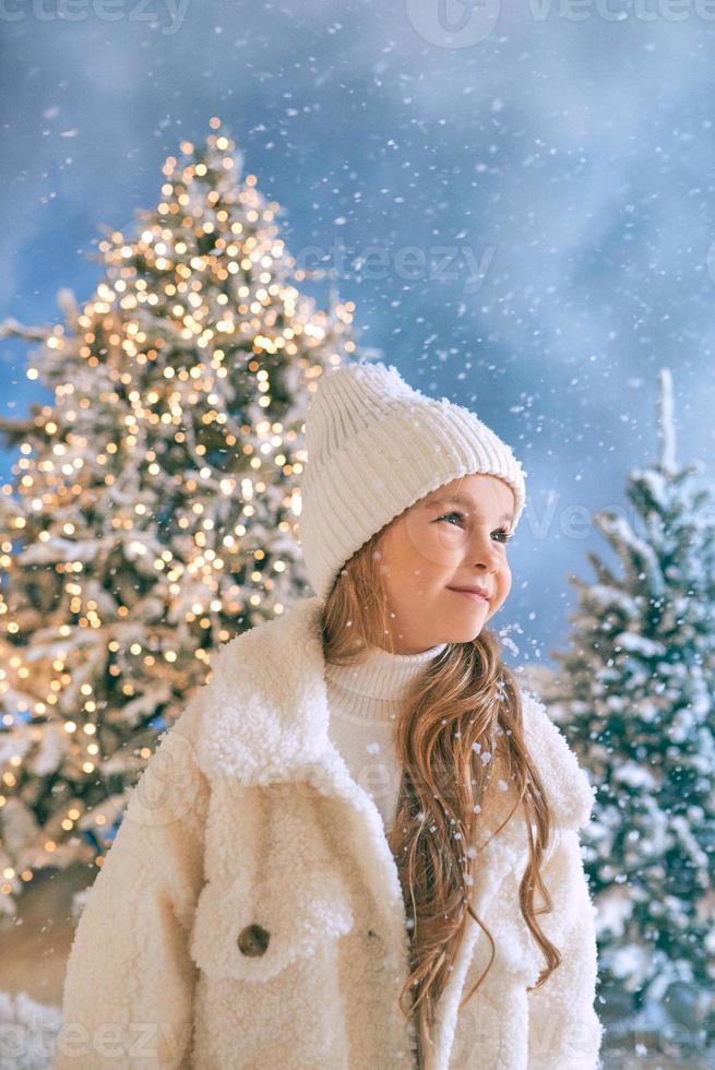 cute caucasian blonde girl in white eco fur coat, hat and gloves walking in the winter christmas forest. New year, fairy tale, fashion concept photo