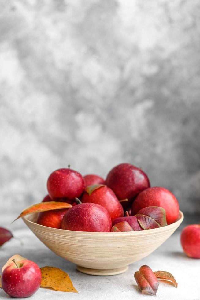 Beautiful fresh red apples with autumn leaves in a wooden vase photo