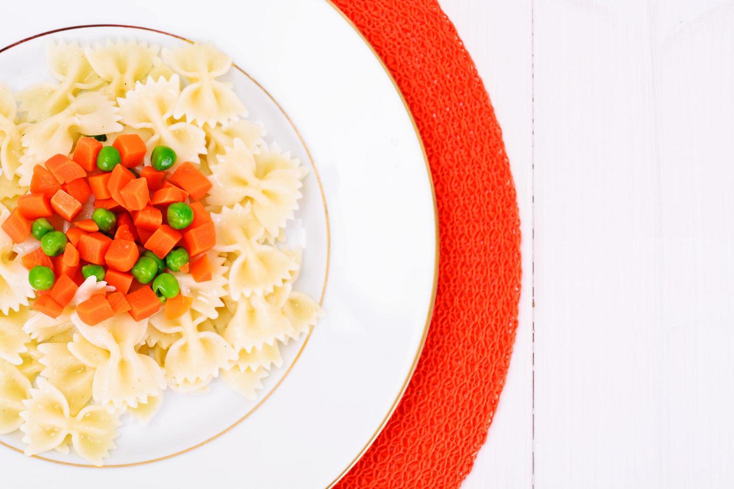 lazo de pasta con zanahorias picadas, salami y guisantes foto