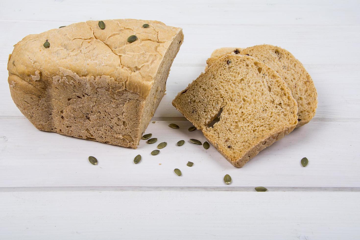 Wheat yeast rustic bread with pumpkin seeds on white wooden board background photo