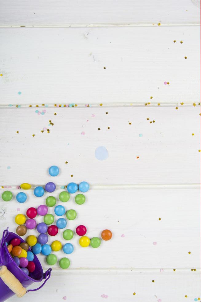 Bombones de caramelo de colores esparcidos sobre fondo de tablero de madera blanca foto