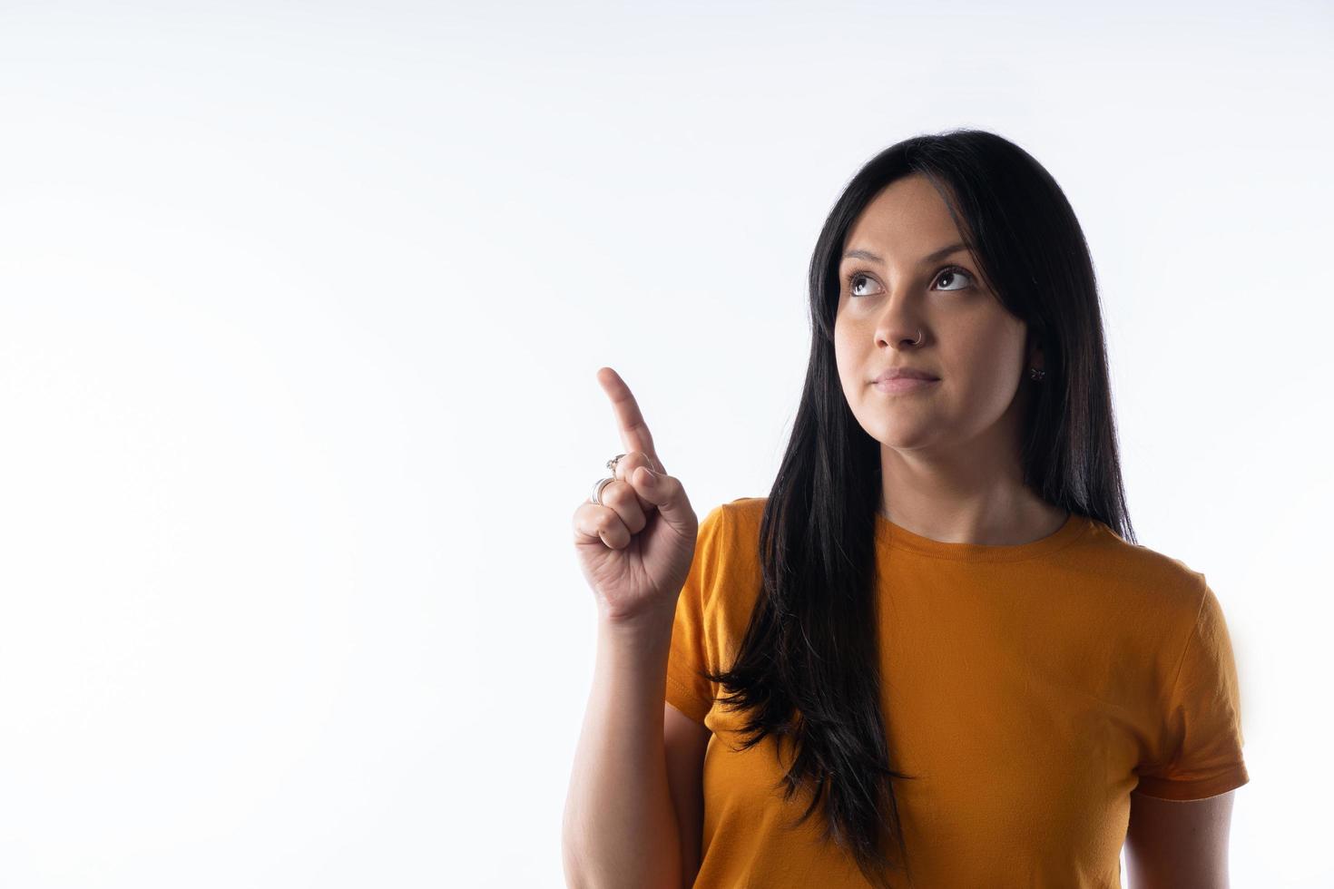 A young Latina woman looks to the left side and points upward. photo