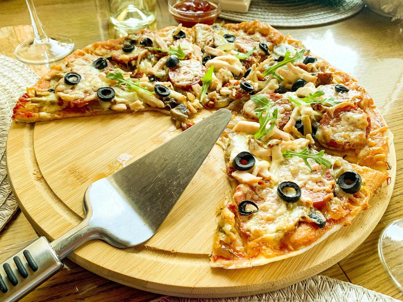Pizza casera en rodajas con salami y aceitunas sobre placa de madera foto