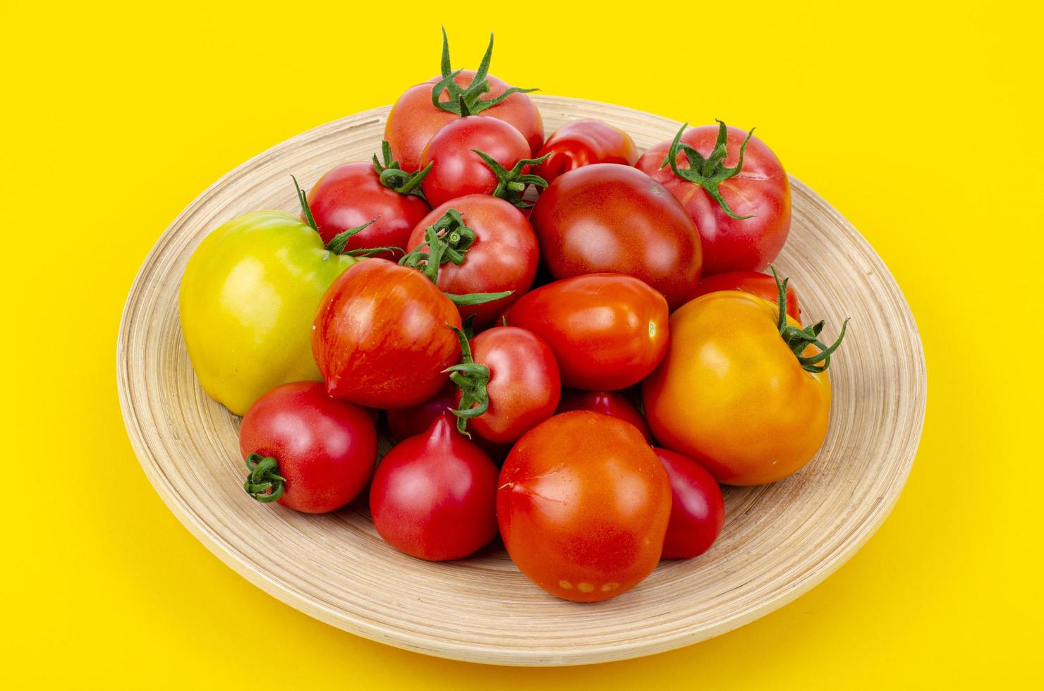 Mix of ripe colorful tomatoes on bright yellow background. Studio Photo