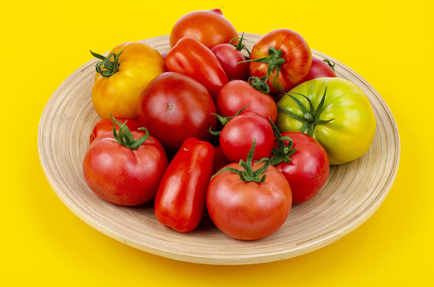 Mix of ripe colorful tomatoes on bright yellow background. Studio Photo