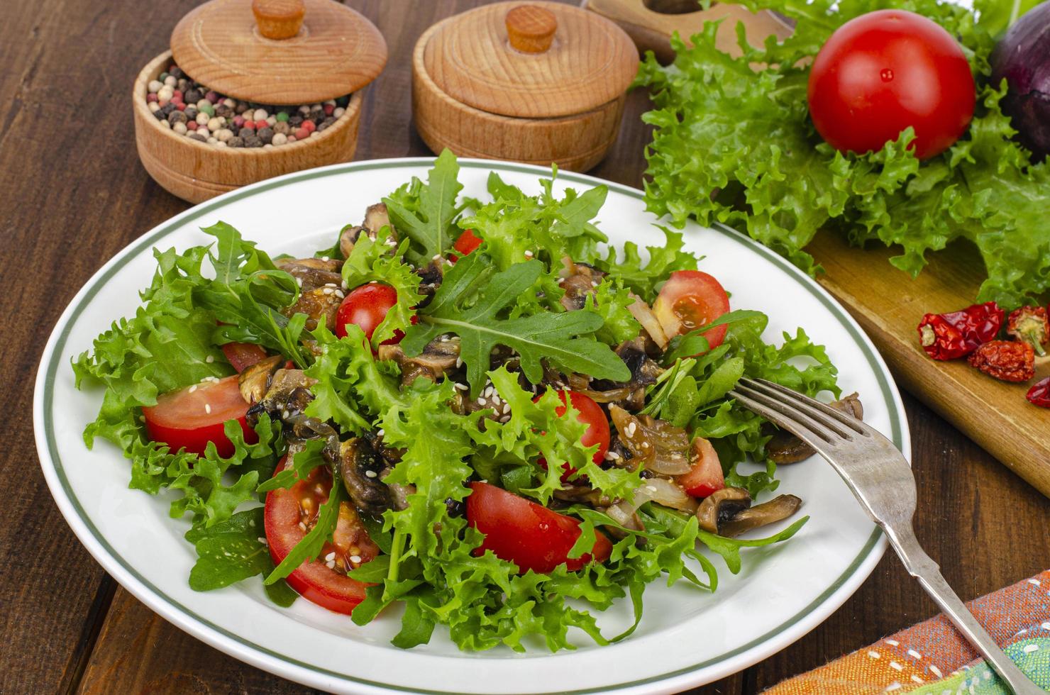 Ensalada de dieta de hojas de rúcula, tomates y champiñones fritos en la mesa de madera. foto de estudio