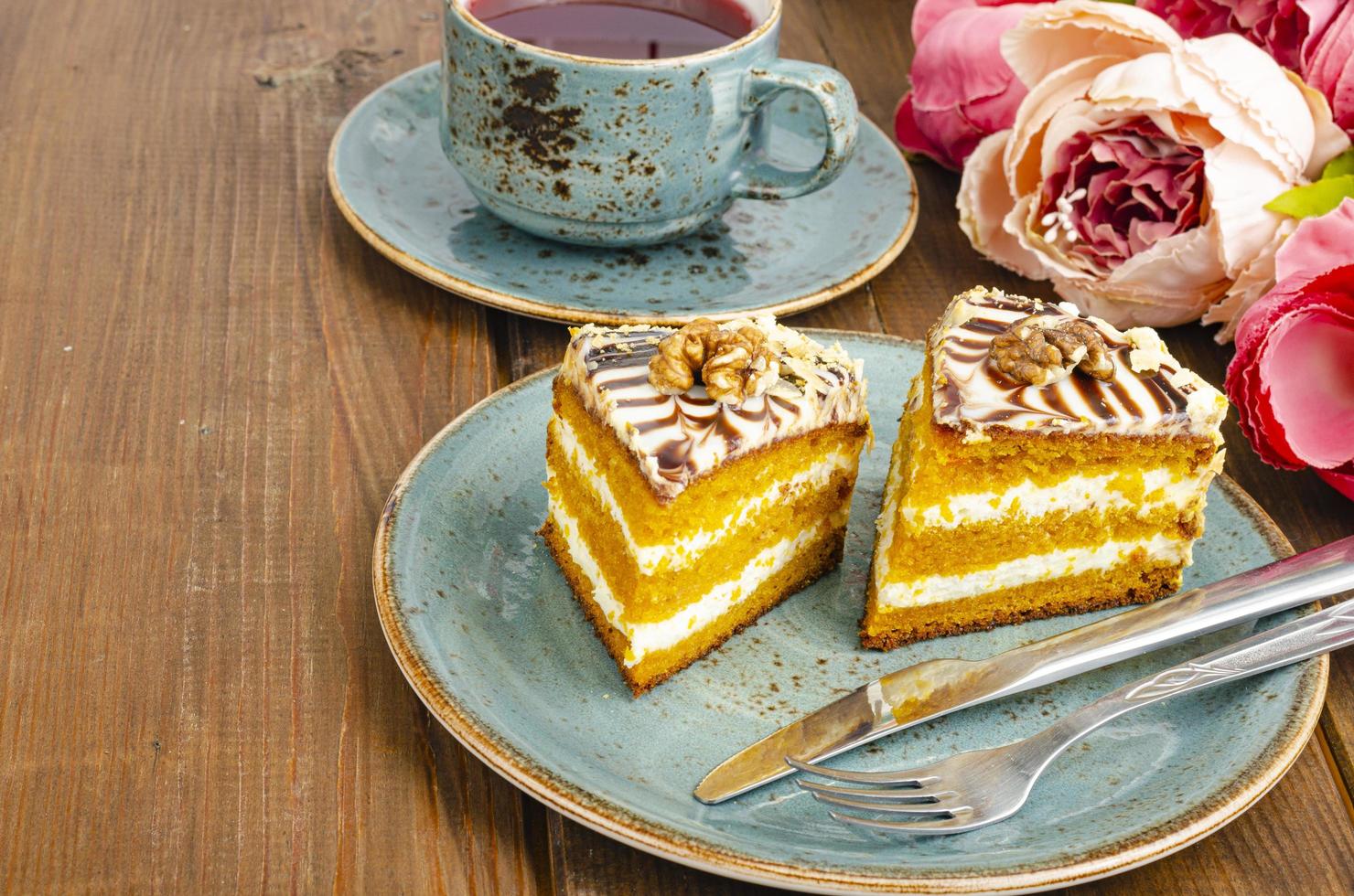 Two pieces of carrot cake on blue plate, cup of tea on wooden table photo
