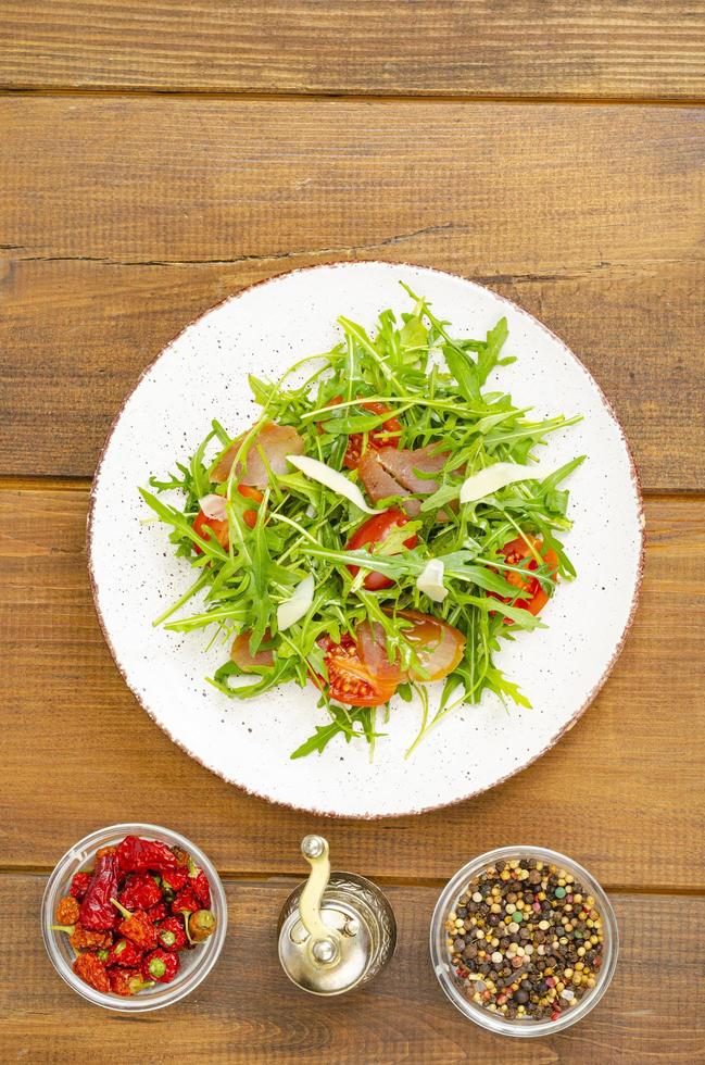 Dish of arugula, tomatoes, dried meat and cheese. Salad on plate on wooden background photo