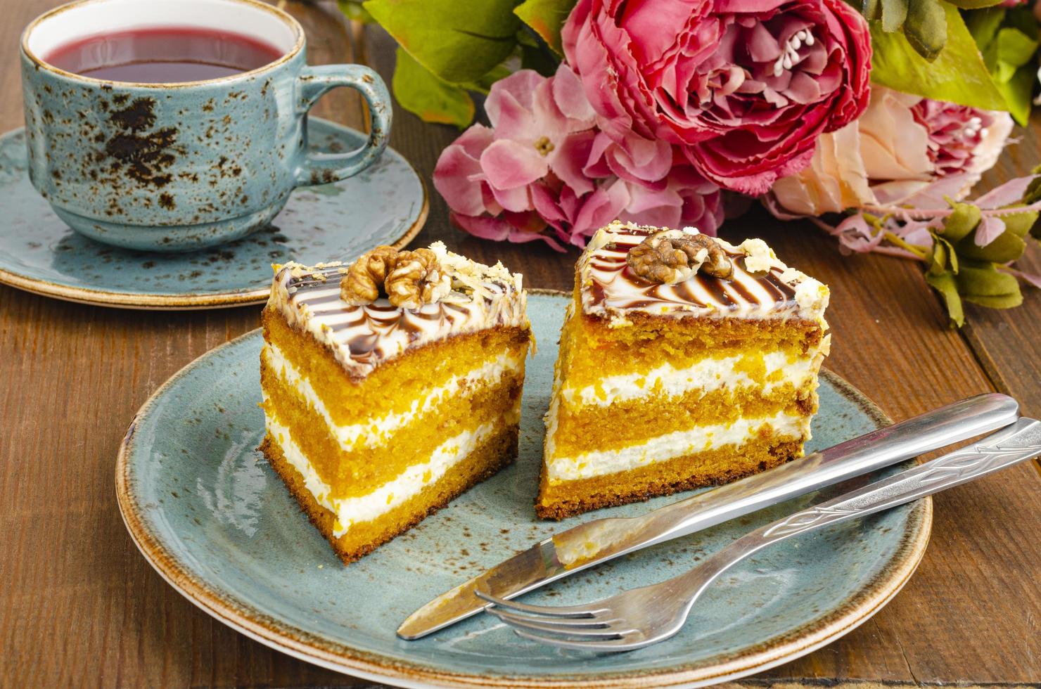 Dos trozos de tarta de zanahoria en la placa azul, una taza de té en la mesa de madera foto