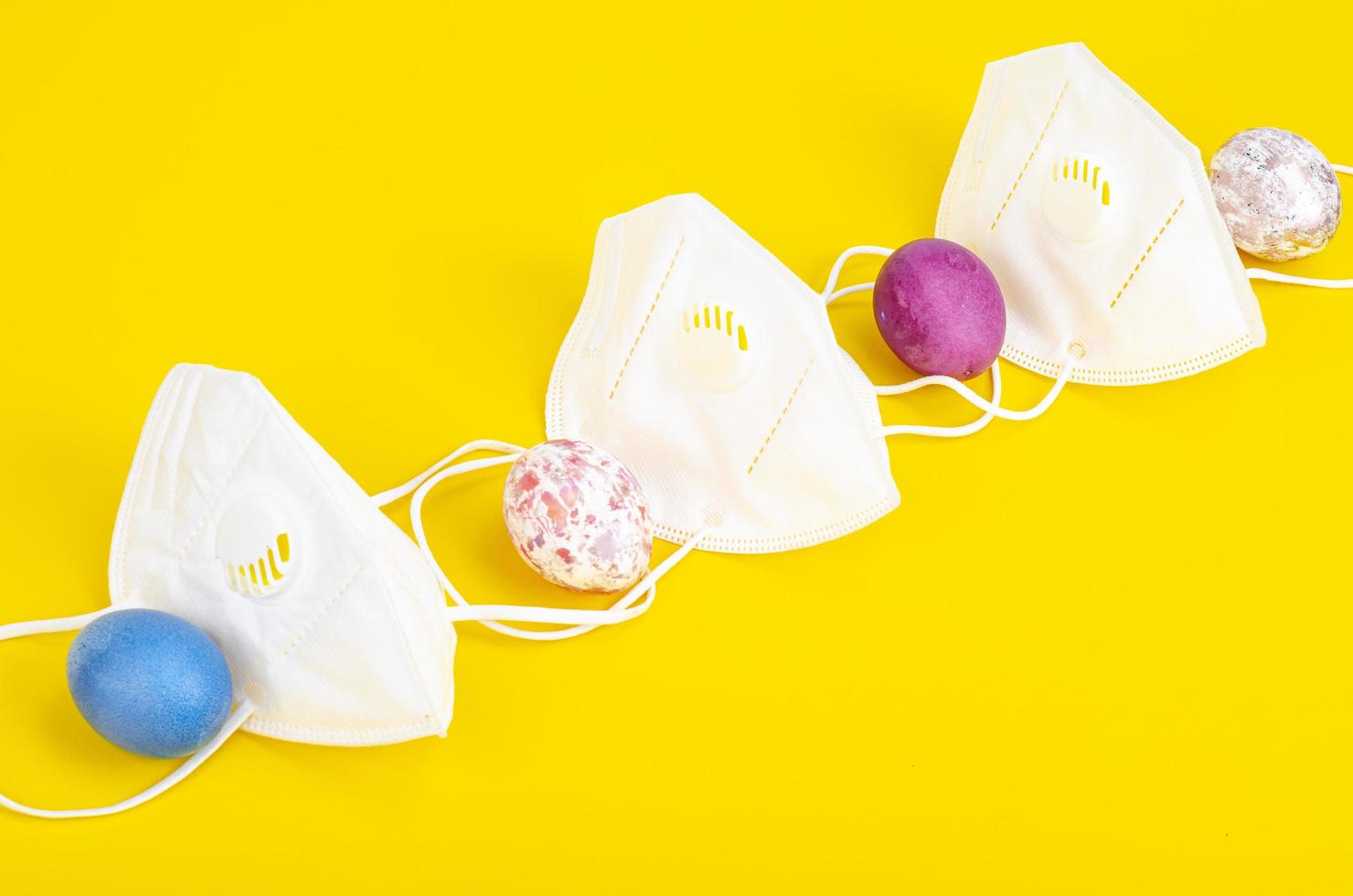 Concept of quarantine at Easter. Decorative eggs and white protective masks on bright background. Social distancing photo