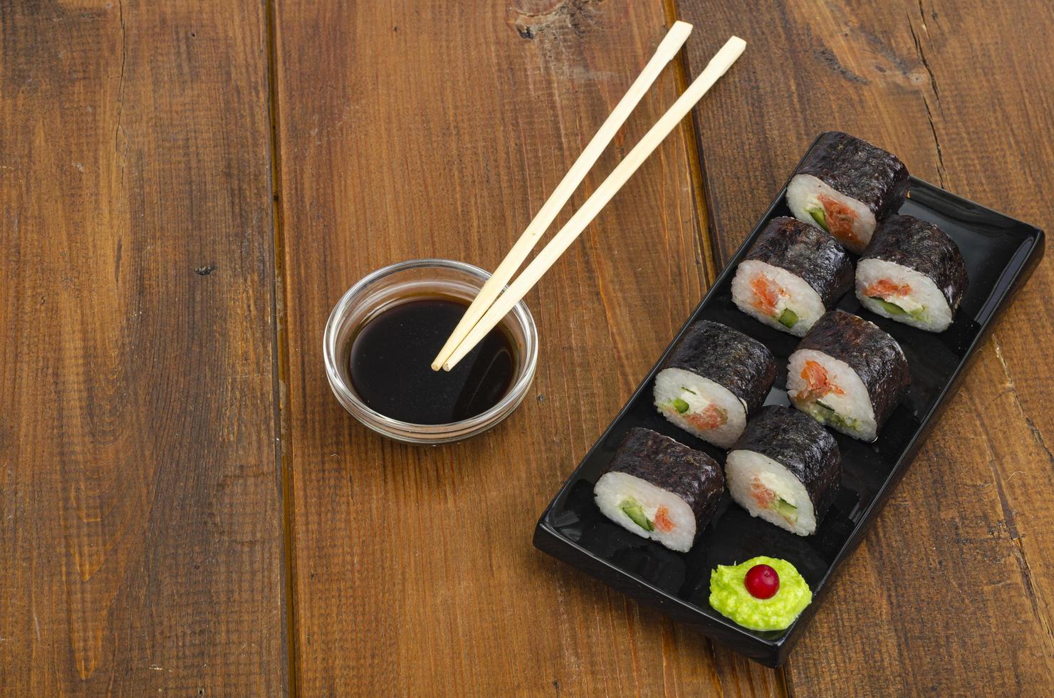 Black plate with rolls with salmon on wooden table. Green wasabi and soy sauce. photo