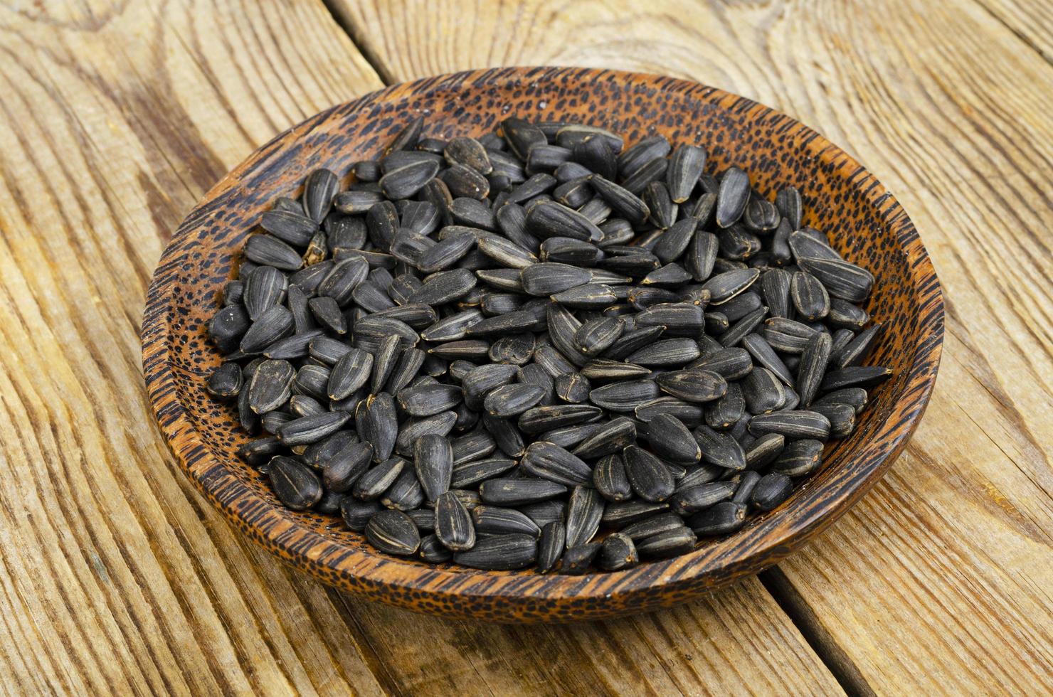 Bowl with sunflower seeds on wooden background. photo