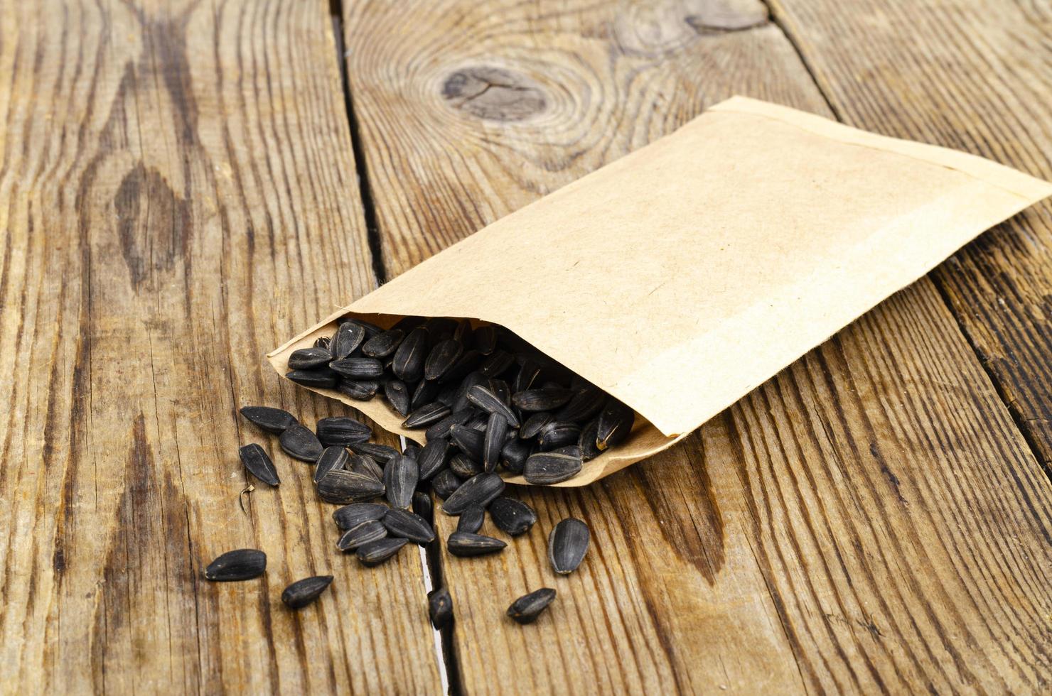 Black unpeeled sunflower seeds in craft bag on wooden table. photo