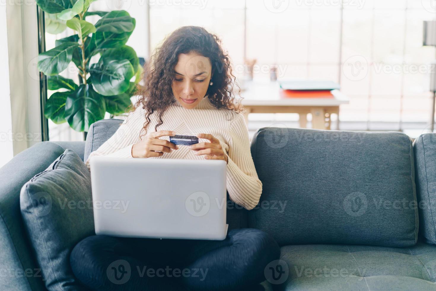 Latin woman using laptop and hand holding credit card for shopping on sofa photo