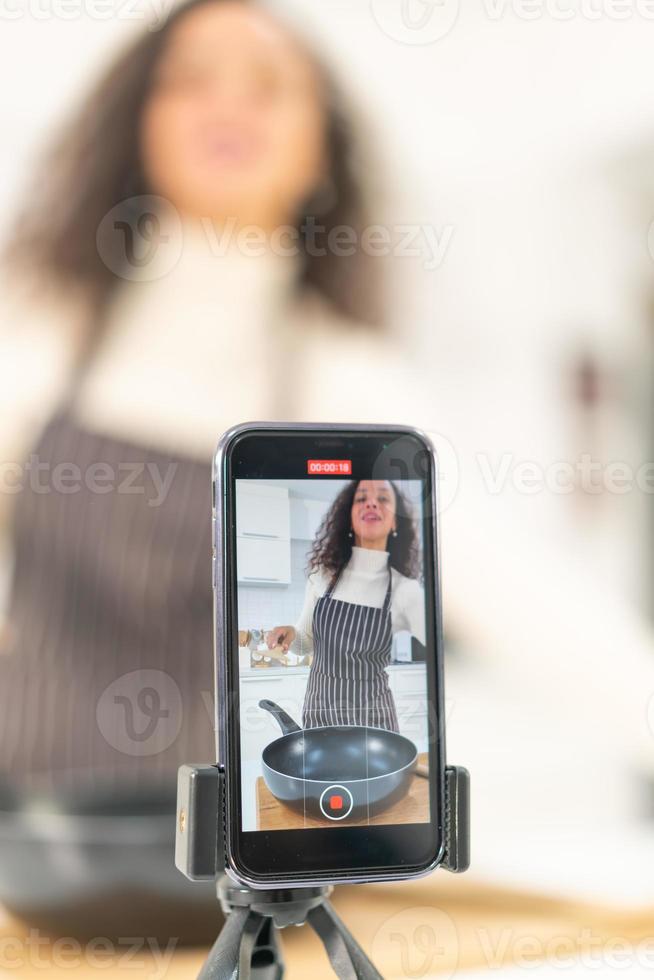 mujer latina grabando video y cocinando en la cocina foto