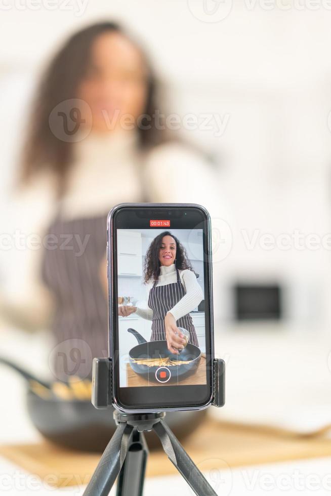 mujer latina grabando video y cocinando en la cocina foto