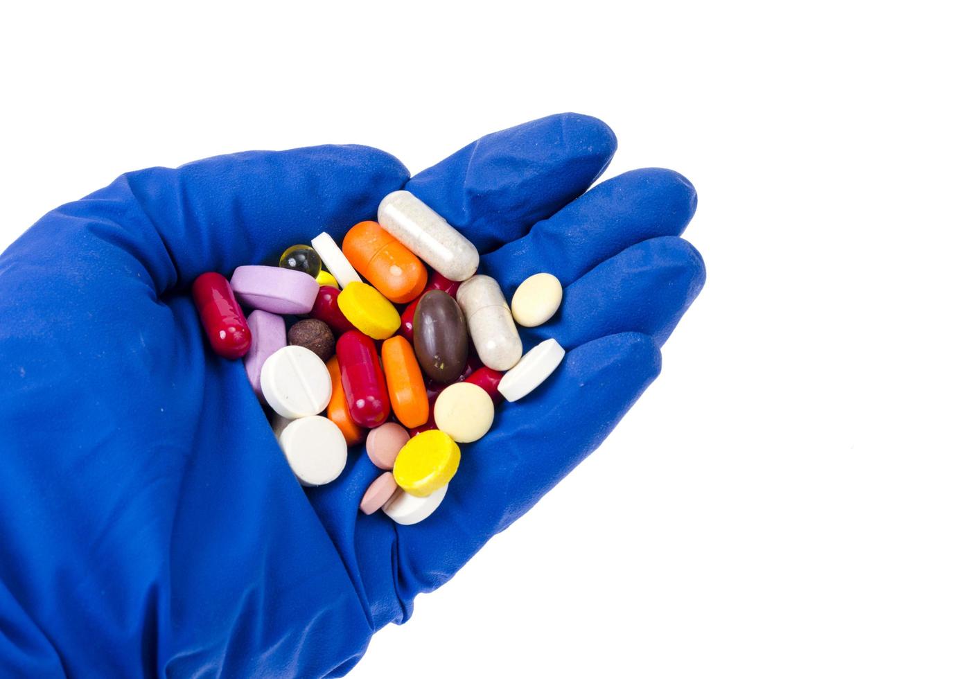 mano en guante médico tiene píldoras, píldoras y cápsulas de colores. foto