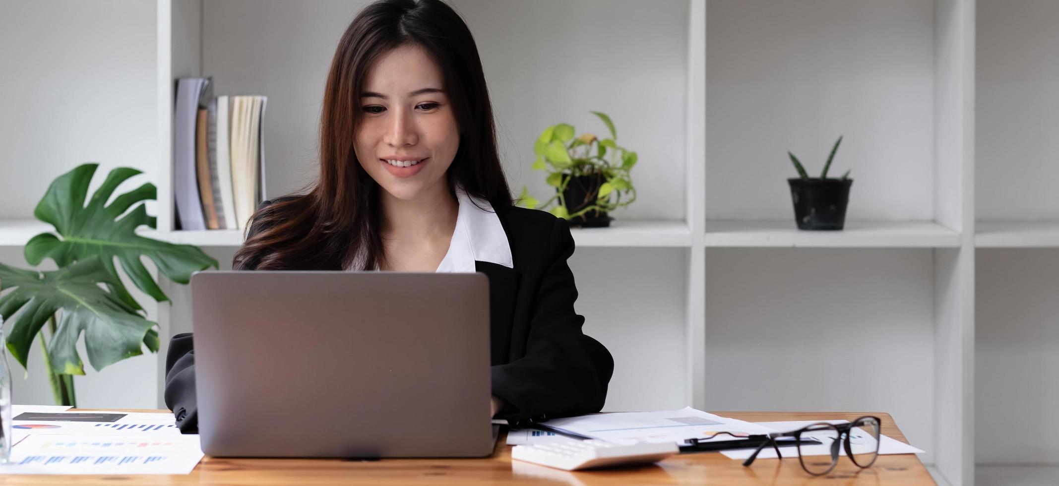 Business asian woman using laptop for do math finance on wooden desk in office, tax, accounting, financial concept photo