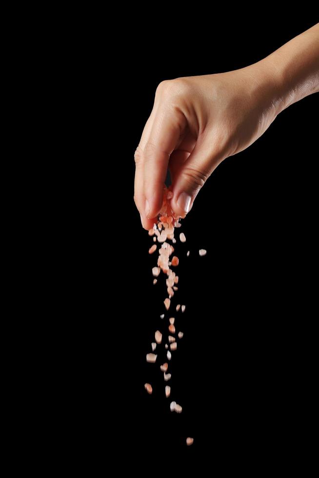 Hand sprinkle pink salt on black background photo