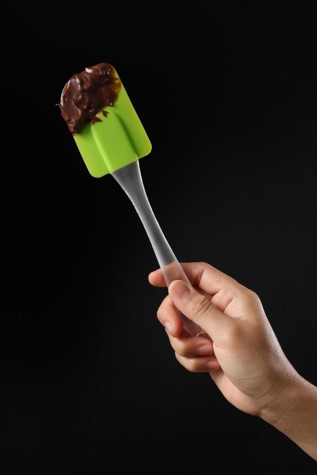 Chef holding spatula and melted chocolate on black background photo