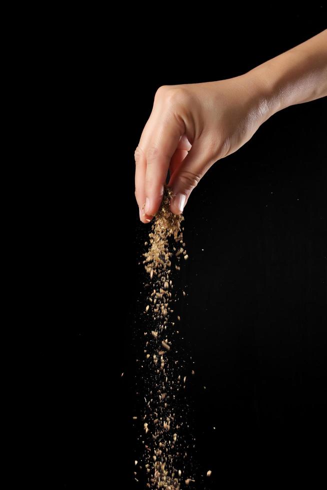 Hand sprinkling oregano on black background photo