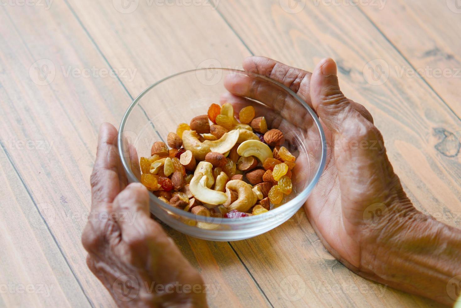 mano de las mujeres mayores sostenga un tazón de muchas nueces mixtas foto