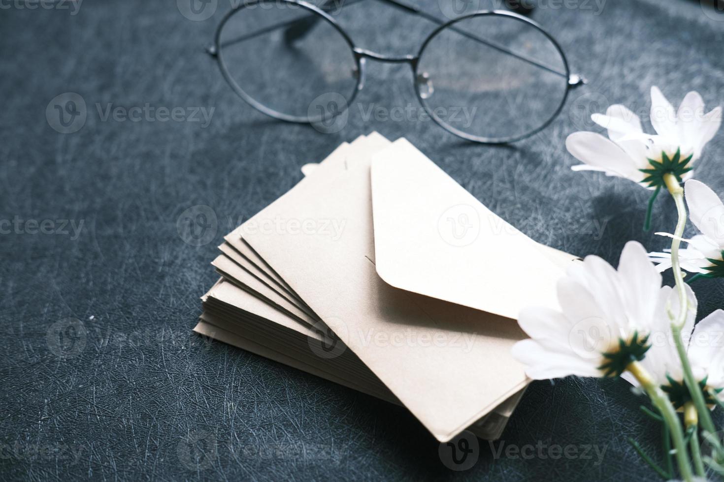 stack of envelope, eyeglass and flower on black background photo