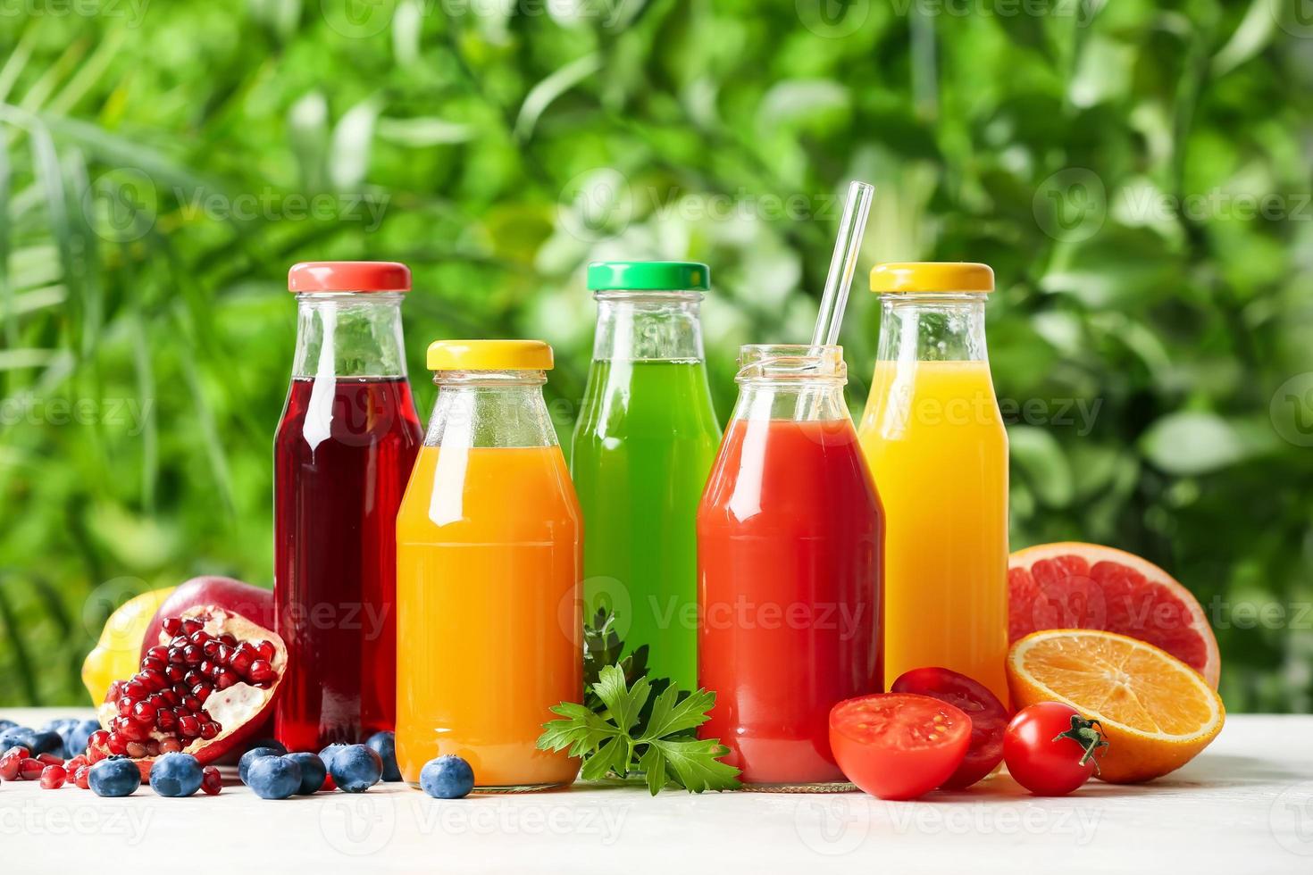 Bottles with healthy juice, fruits and vegetables on table outdoors photo