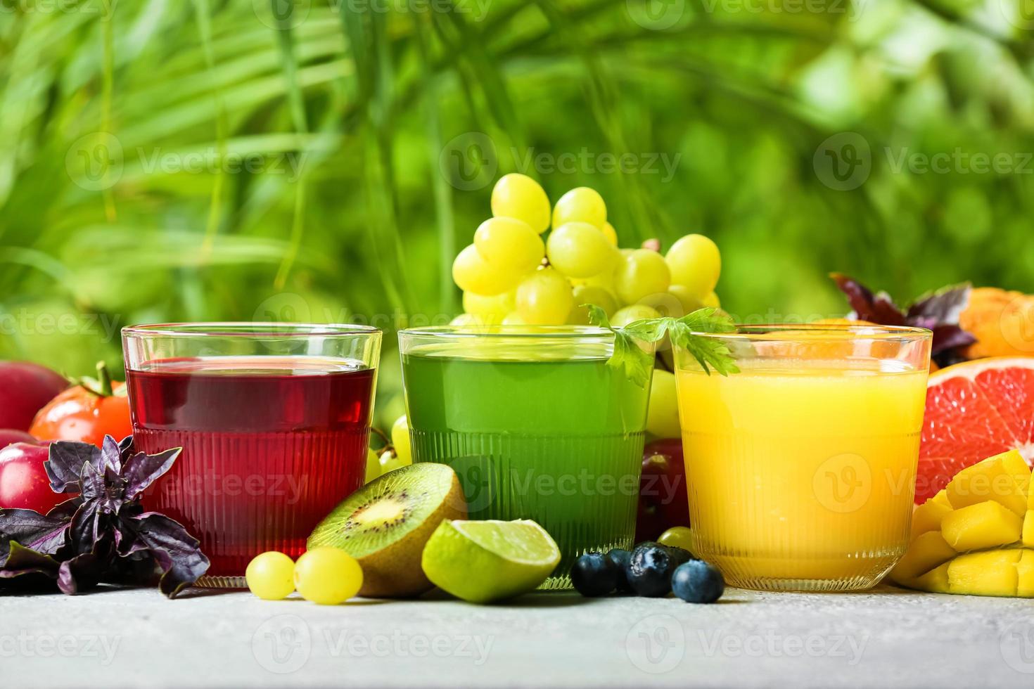 Glasses with healthy juice, fruits and vegetables on table outdoors, closeup photo