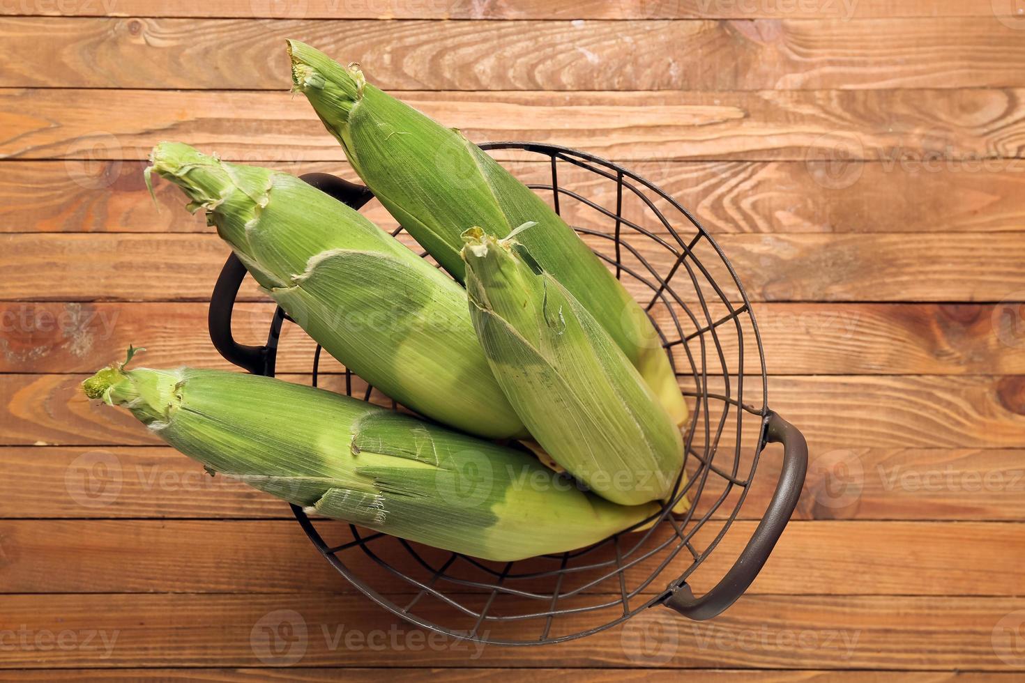 Cesta con mazorcas de maíz frescas sobre fondo de madera foto