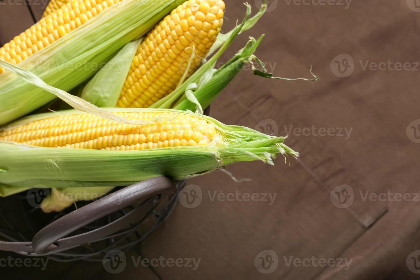 Cesta con mazorcas de maíz frescas sobre fondo de tela, primer plano foto