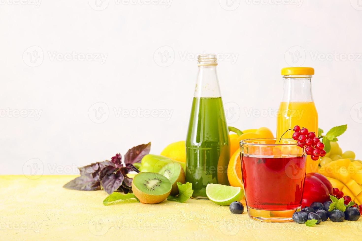 Botellas con jugos saludables, frutas y verduras sobre fondo claro foto