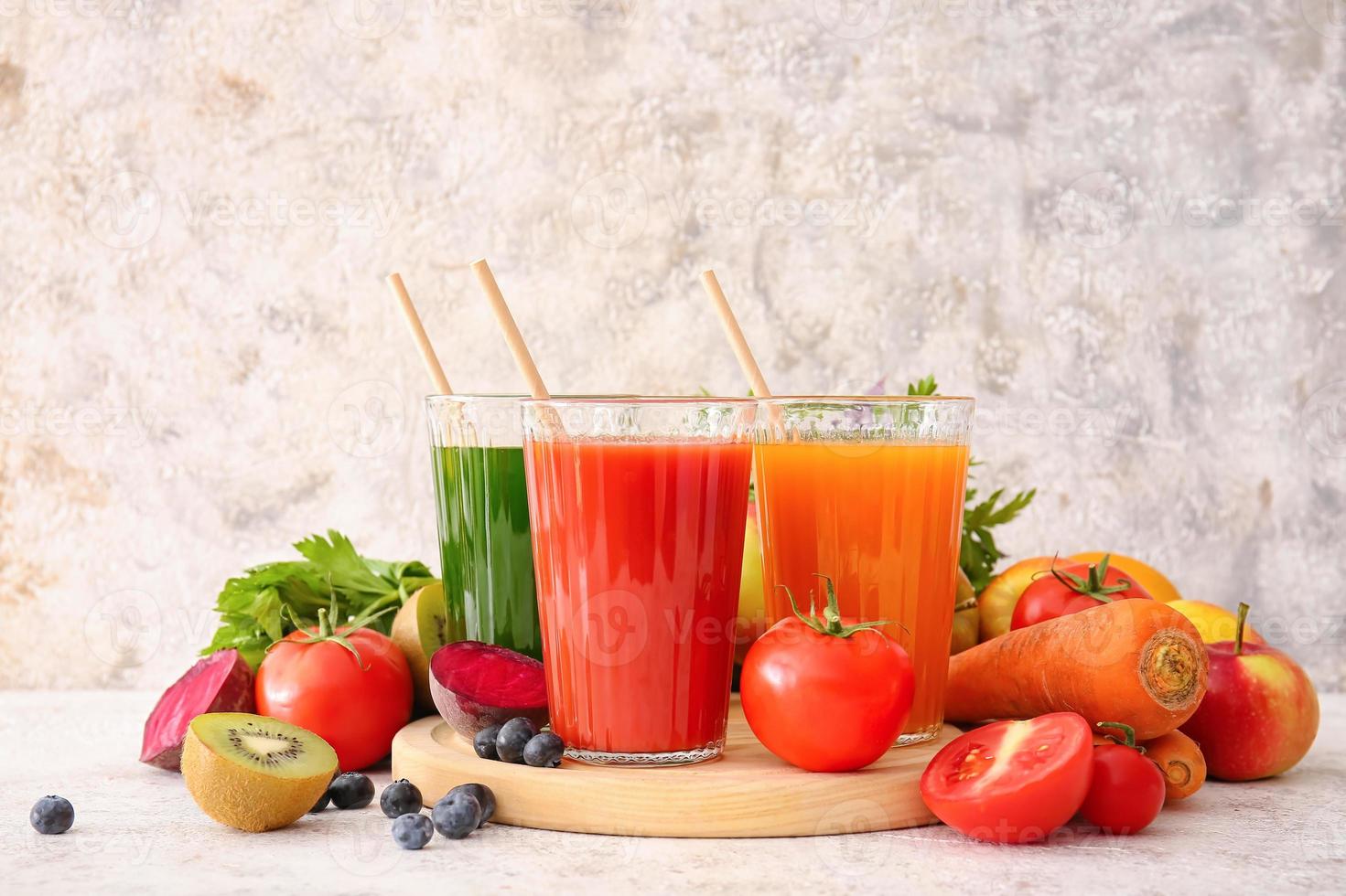 Glasses with healthy juice, fruits and vegetables on light background photo
