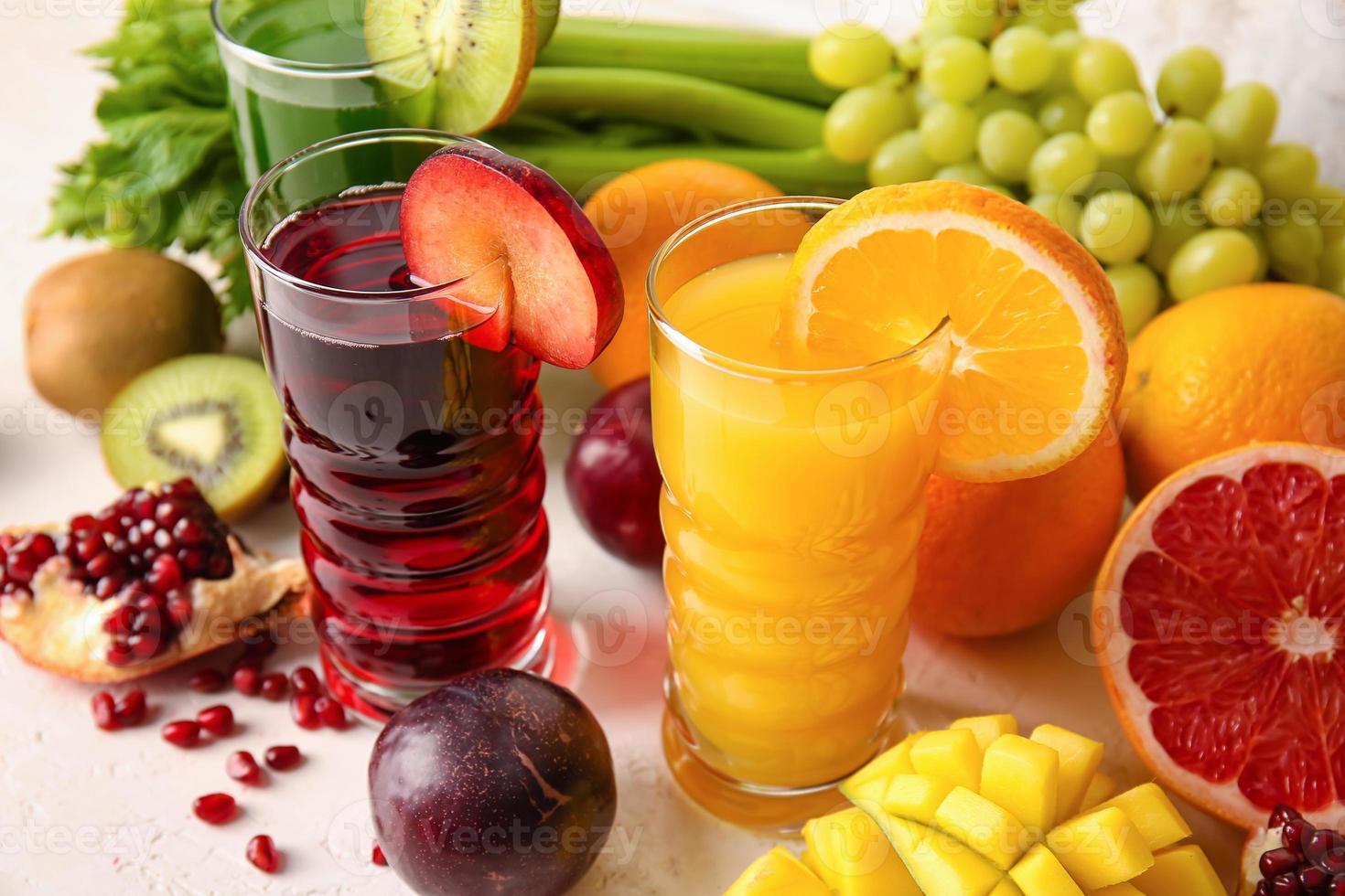 Glasses with healthy juice, fruits and vegetables on light background photo