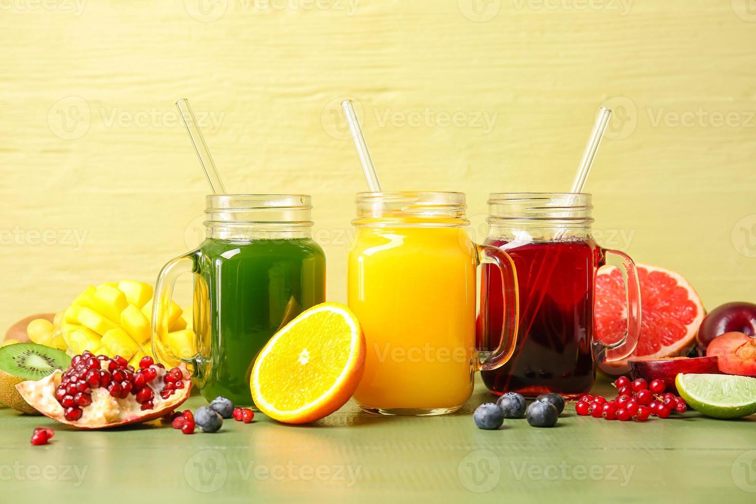 Mason jars with healthy juice, fruits and vegetables on color wooden background photo