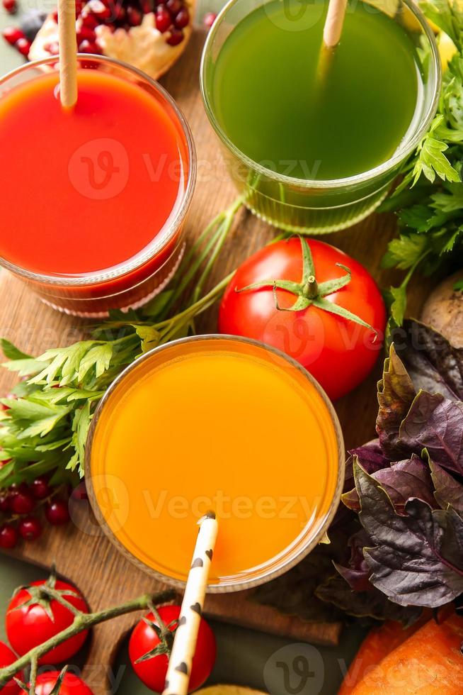 Glasses with healthy juice, fruits and vegetables on color wooden background photo