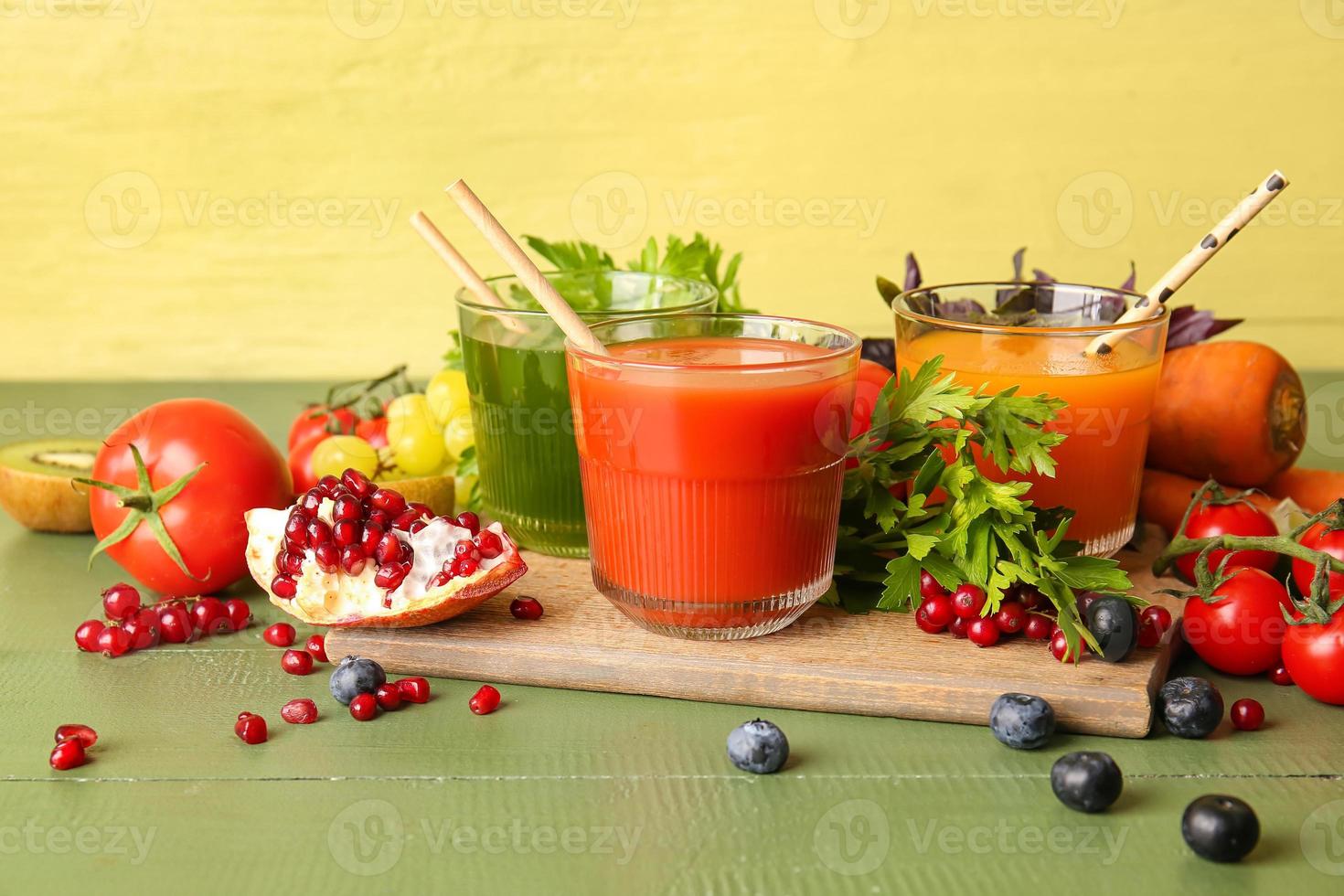 Glasses with healthy juice, fruits and vegetables on color wooden background photo