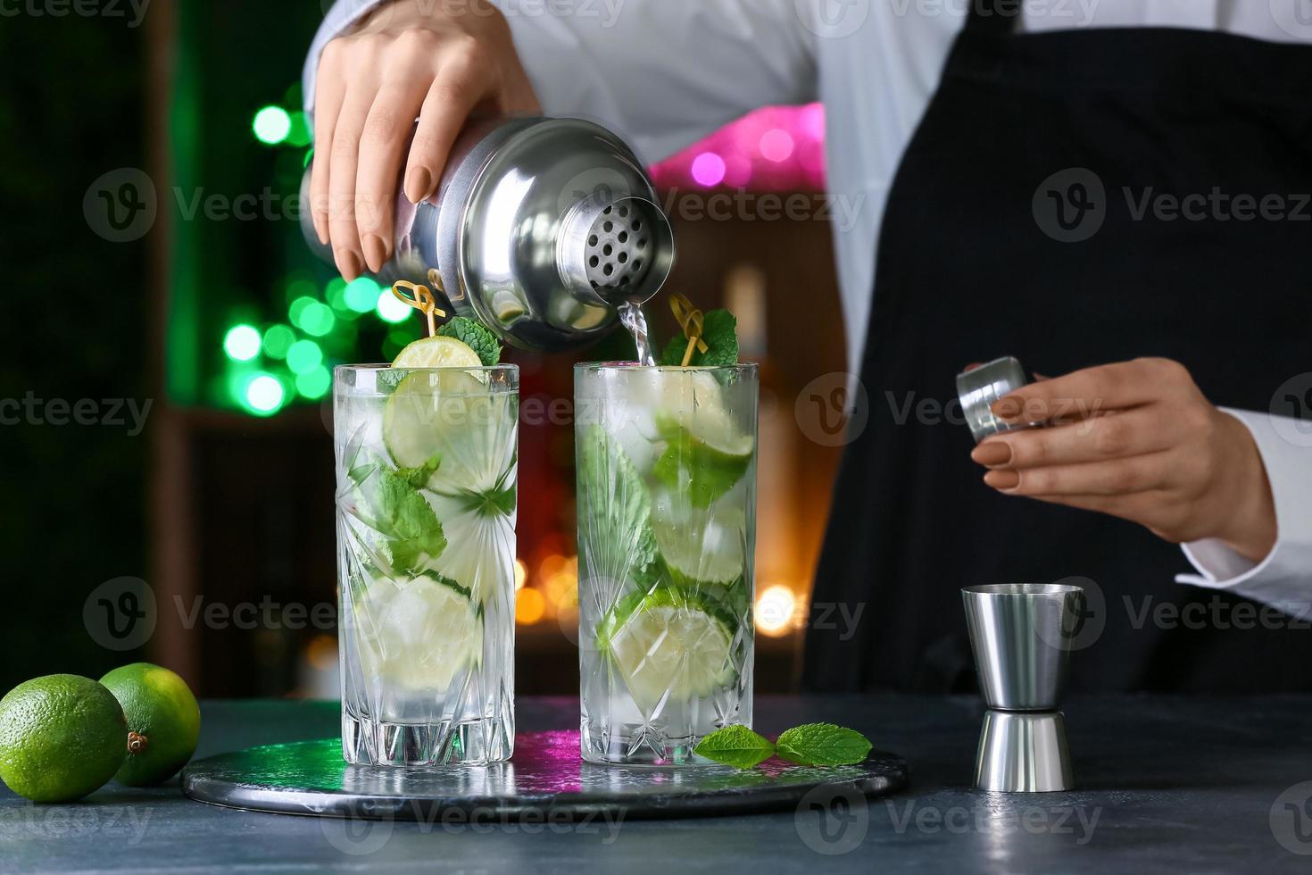 Female bartender making fresh mojito on table in bar photo