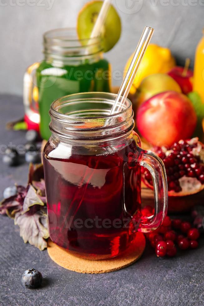 Frascos de albañil con jugos saludables, frutas y verduras sobre fondo oscuro foto