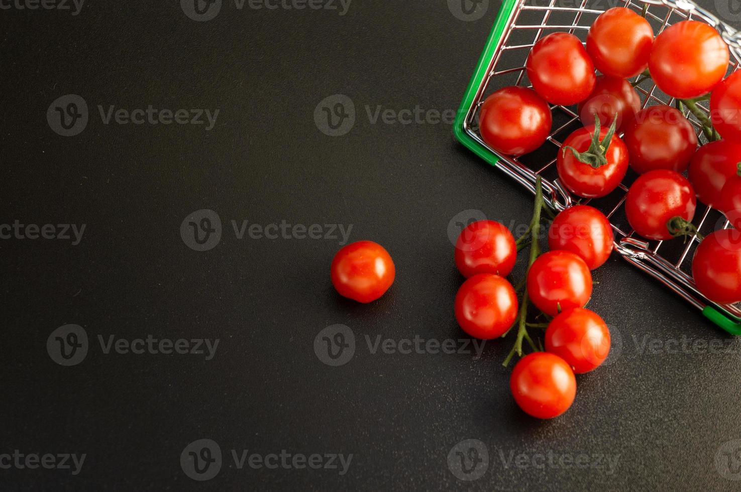 Scattered cherry tomatoes in a basket against a black background with an empty place for an inscription. photo